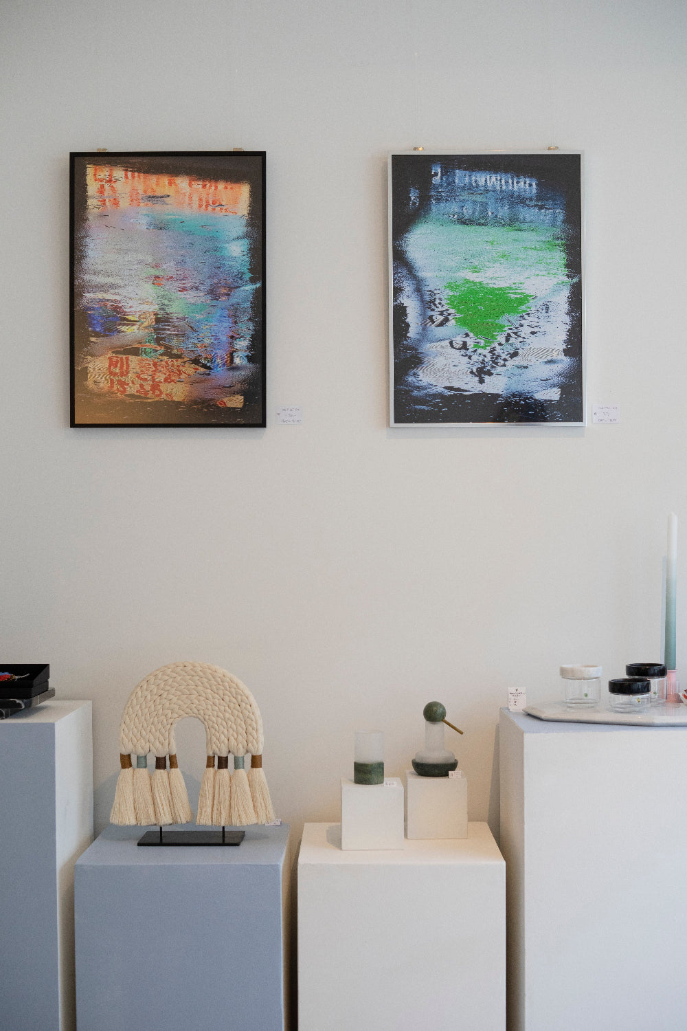 Two abstract paintings on a wall with decorative items on white pedestals.